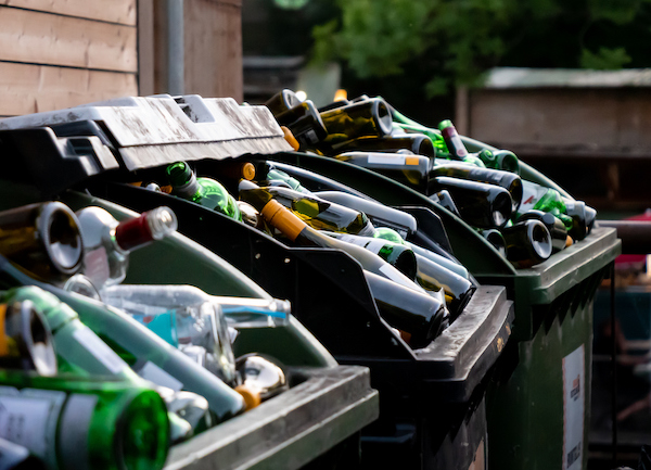 Lots of empty glass bottles in different colors disposed of in commercial recycling containers.