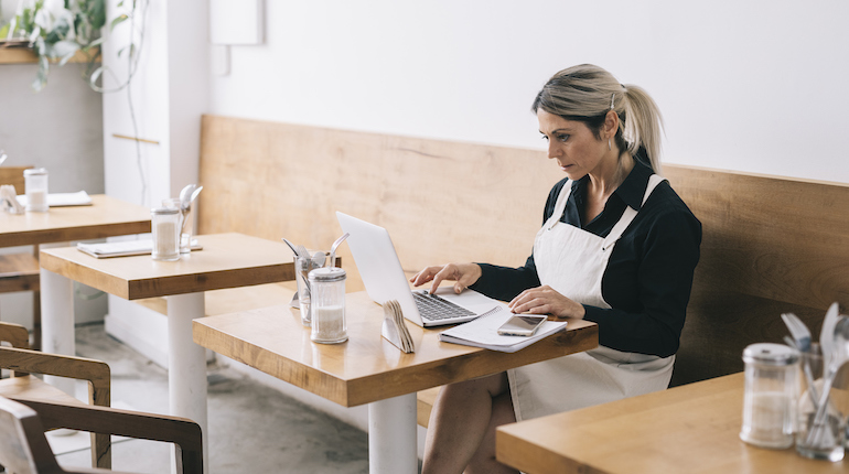 Manager paying bills and wages on a laptop in a cafe.