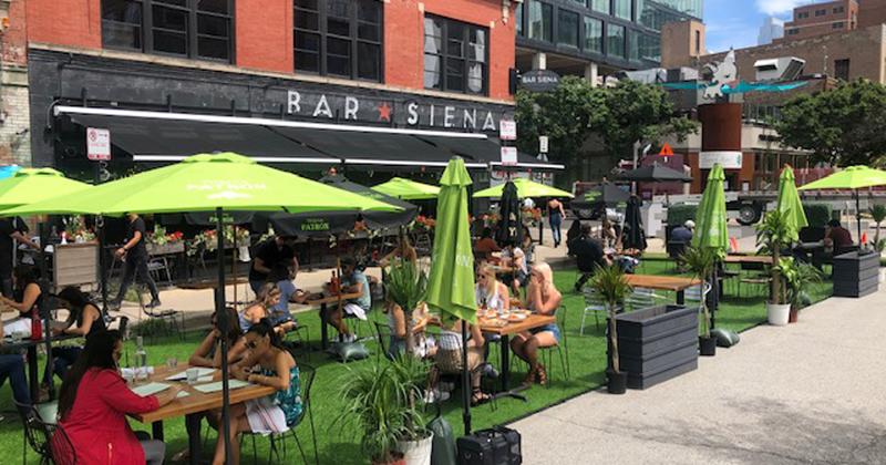 The patio of Bar Siena in Chicago, which features fake grass, plants, and bright green umbrellas.