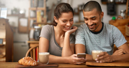 Shot of a young couple using a cellphone while sitting in a coffee shop.
