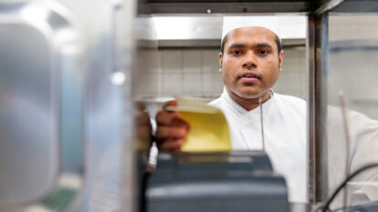 A man in a white chef hat and uniform receiving an order from the restaurant.