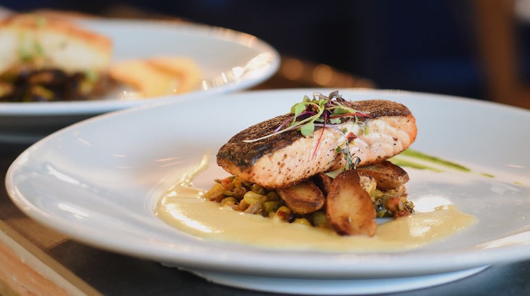 Salmon filet garnished with pea shoots and sitting on a bed of lentils.