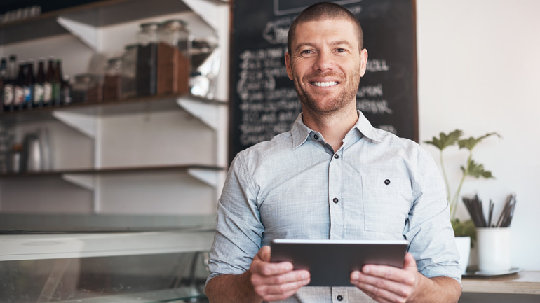 A man wearing a pale blue dress shirt holding a tablet in a restaurant.