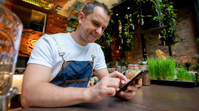 Cheerful waiter taking a break at work by checking his social media on his phone.