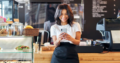 Portrait of smiling waitress barista using mobile phone at work.