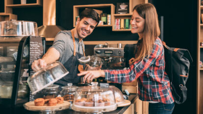 Woman standing at the counter talking to a man who works at the cafe and is looking to buy muffins.