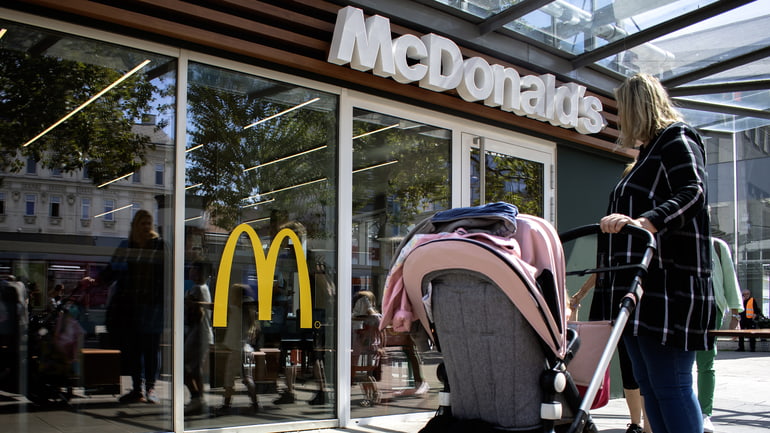 Woman wearing a black and white coat standing in front of a McDonalds with a pink and gray baby stroller.