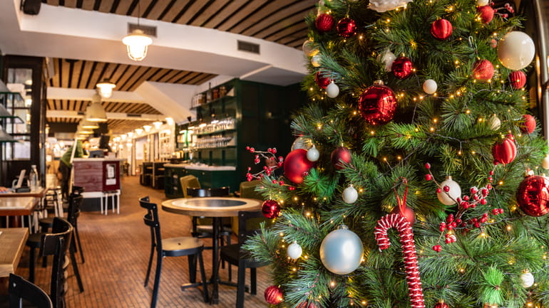 Green Christmas tree with red and white decorations inside a restaurant.