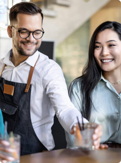 Two people smiling as one hands the other a drink