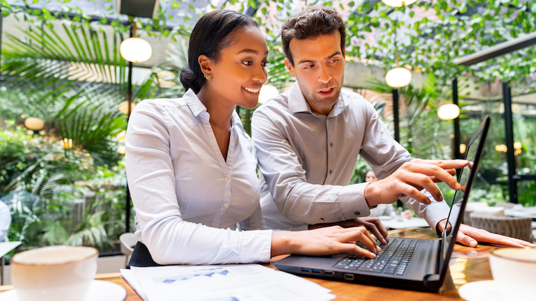 Two restaurant staff working in front of a laptop at a restaurant.