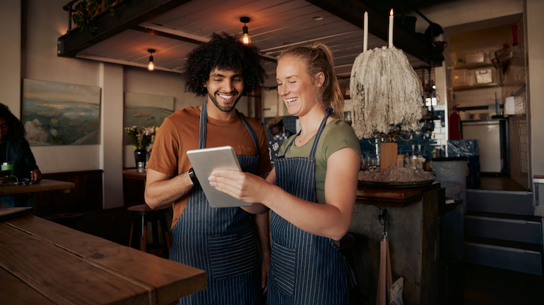 Two restaurant workers chatting and looking at a tablet.