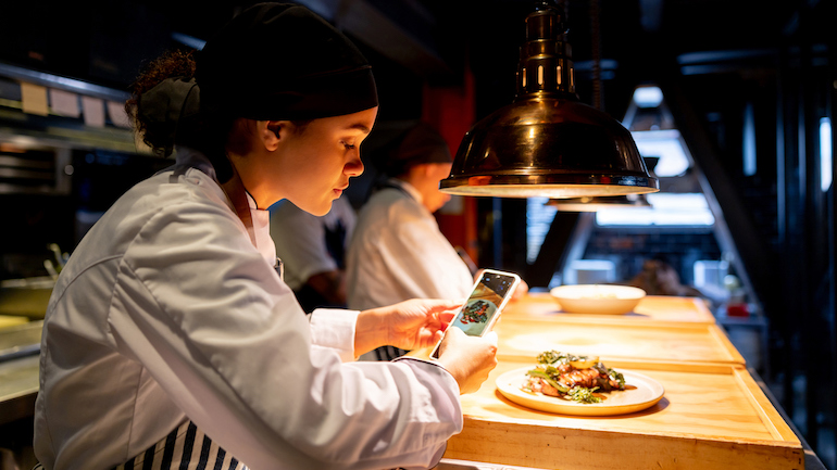 Chef taking a photo of a plate of food with her phone.