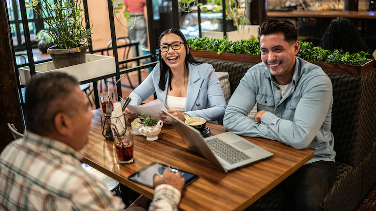 Three people sitting at a restaurant having a business meeting.