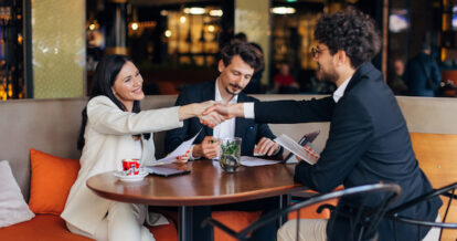 Three business people coming to an agreement and shaking hands while at a restaurant.