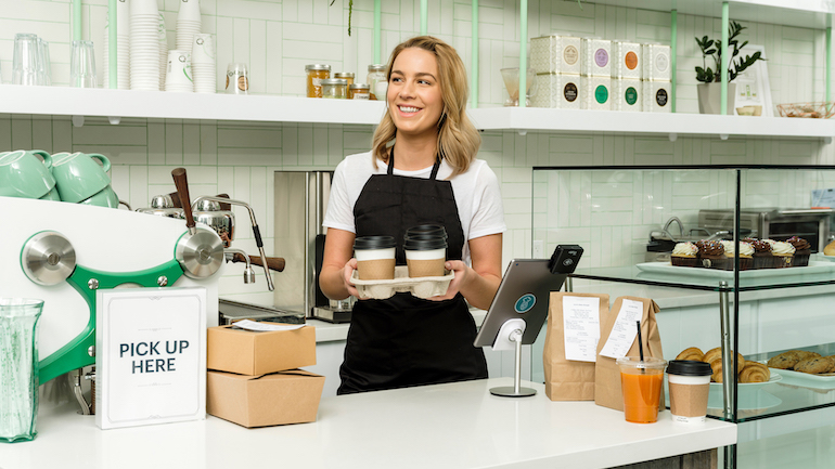 Cafe worker holding a tray of three to-go drinks ready for pick-up.