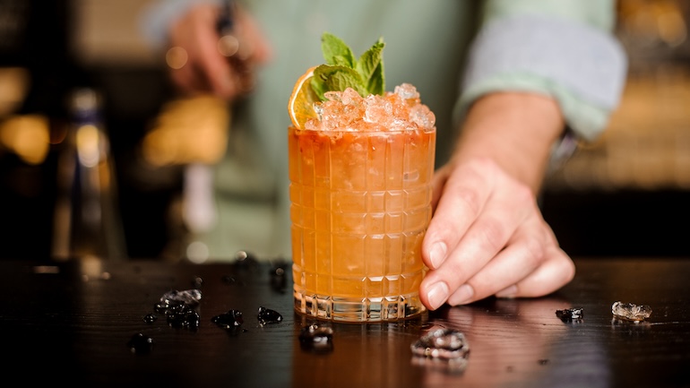 A close up of an orange drink garnished with an orange slice and mint.