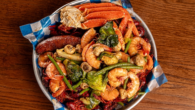 Silver platter filled with a seafood boil, including shrimp, sausage, crawfish, crab legs, and more.