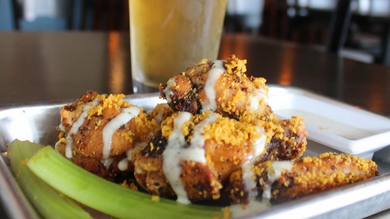 Chicken wings on a silver tray with celery and glass of beer in the background.