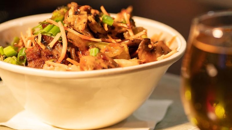 Bowl of food with a glass of beer on a table.
