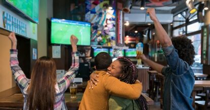 Back view of friends celebrating at a restaurant watching a soccer game.