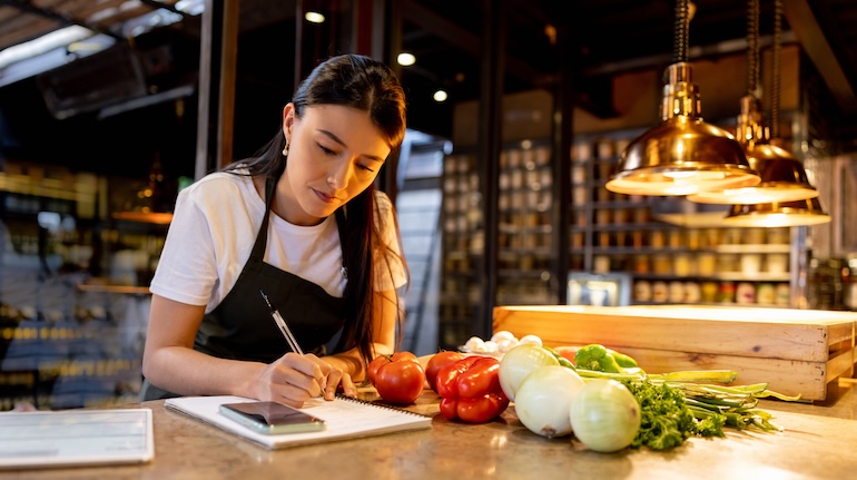 Restaurant working writing menu specials on a notepad next to produce on the table.