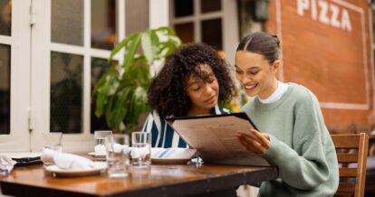 Two people sitting at a table at a restaurant outdoors looking at a menu.