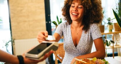 Woman paying for a restaurant meal by tapping her credit card on a credit card terminal.
