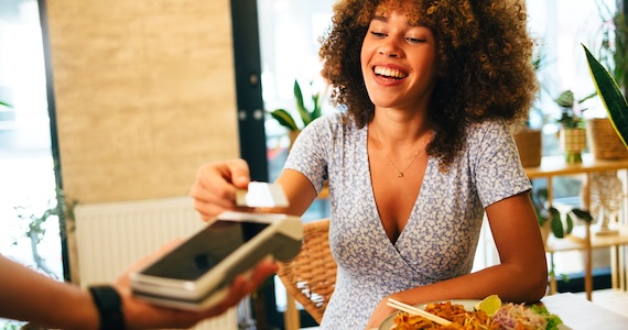 Woman paying for a restaurant meal by tapping her credit card on a credit card terminal.