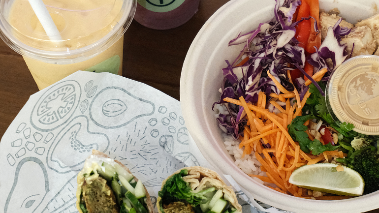 A yellow smoothie, wrap, and bowl on a table.